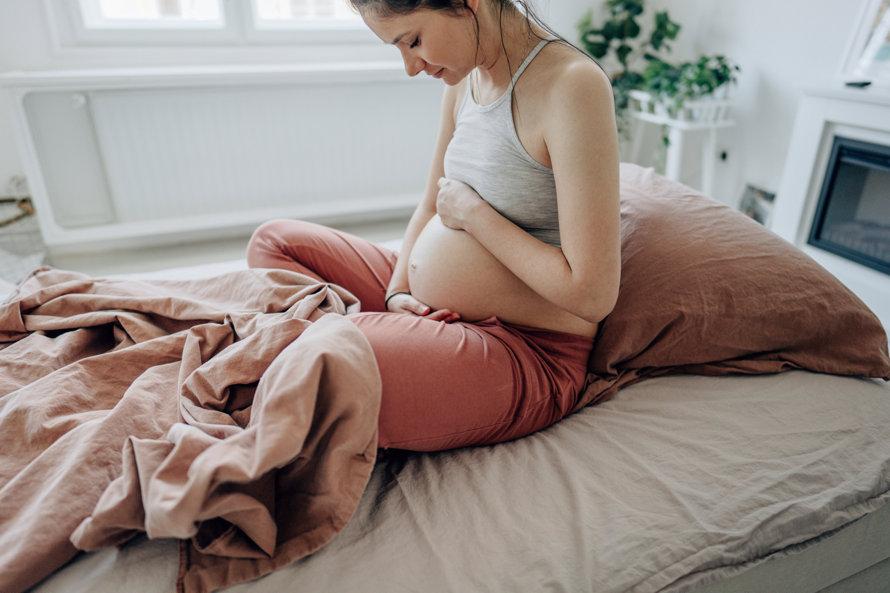 Schwangere auf Bett hält ihren Bauch