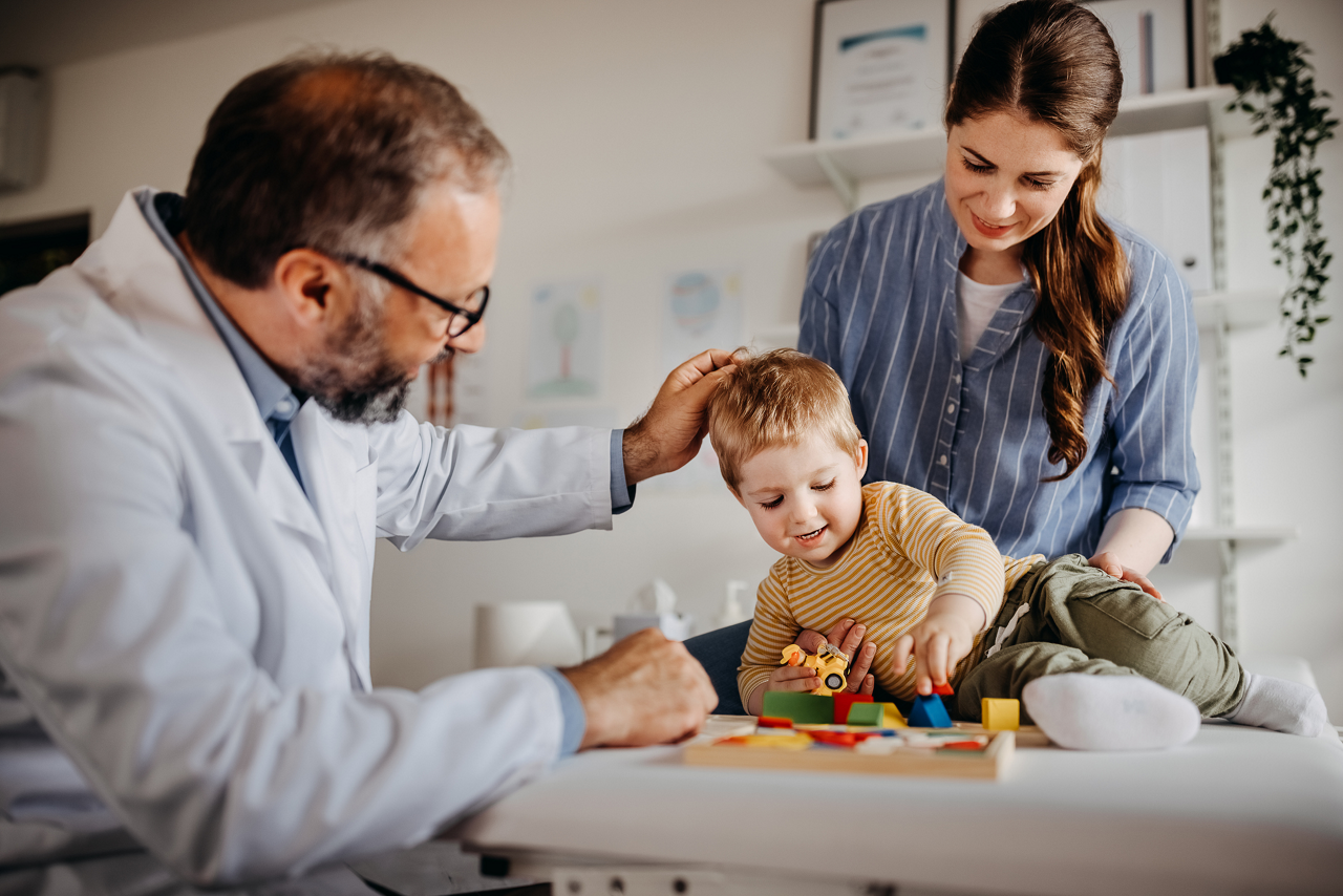 Doctor looking at playing toddler with mother