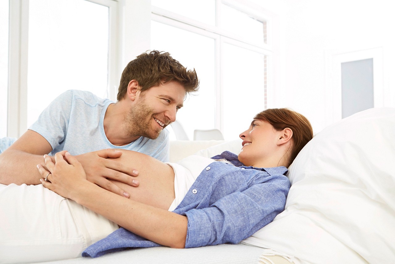 Pregant lady lying on bed with partner feeling bump