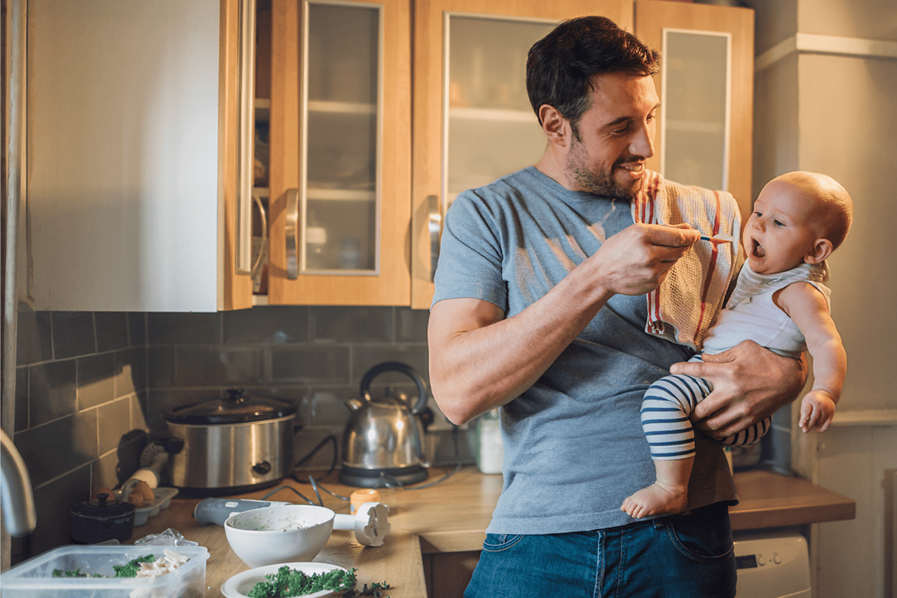 Vater füttern Baby auf seinem Arm einen Löffel Brei
