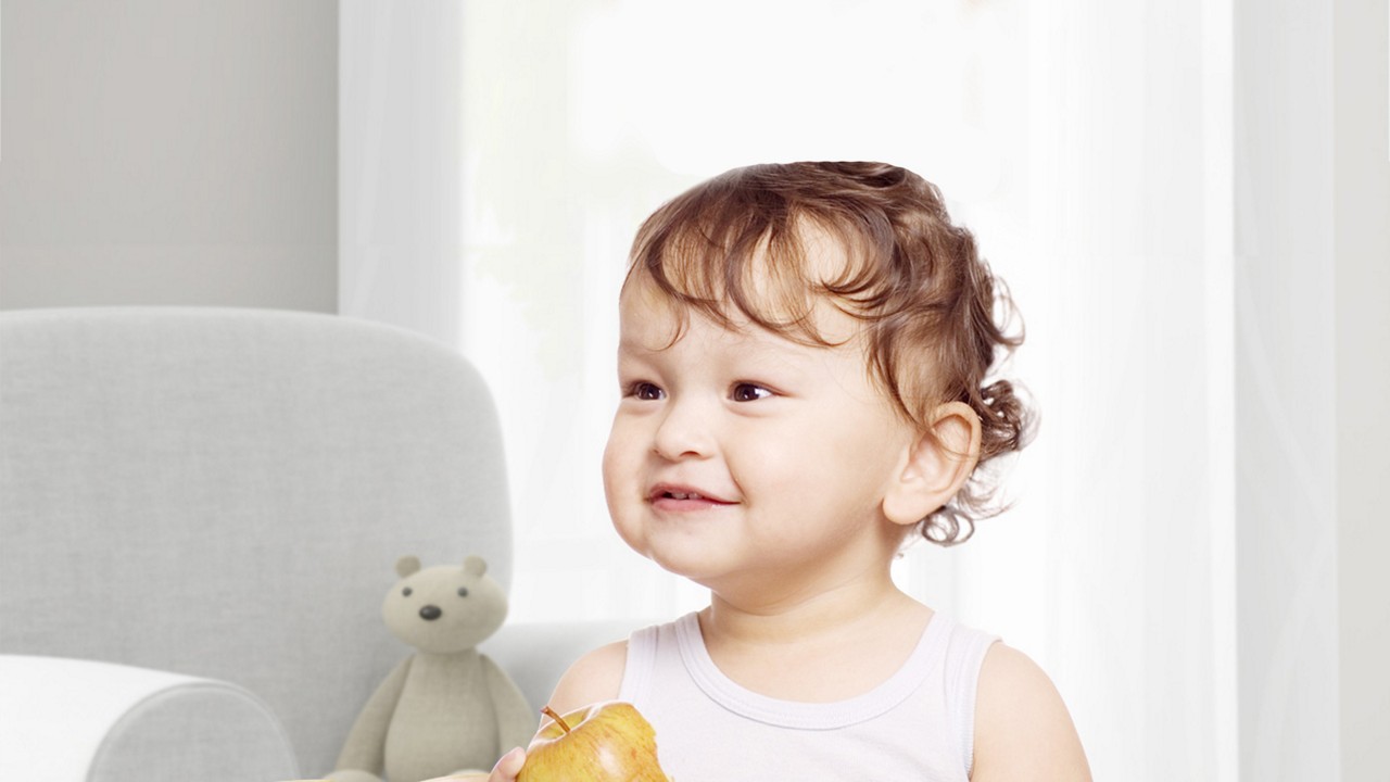 Cute baby girl with curly hair smiles and holds apple
