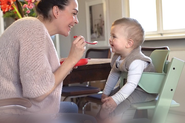  Mutter füttert ihr Baby mit leckerem Babybrei und das Kind hat Freude am Essen