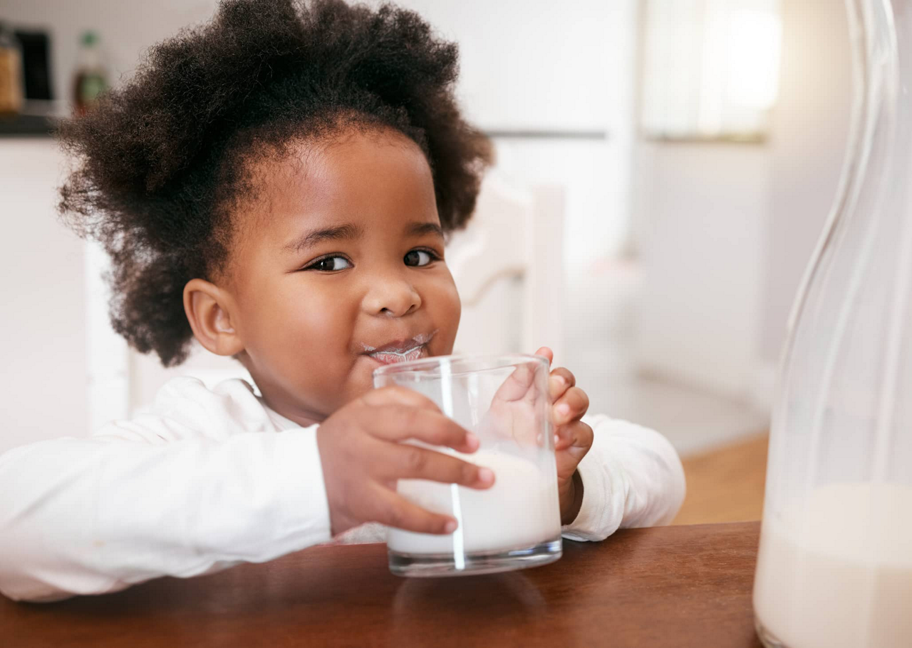 Kind hält Milchglas und trinkt daraus 