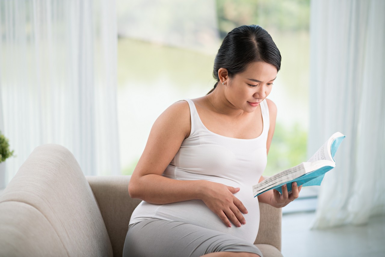 30th-week pregnant woman reading a book on the couch