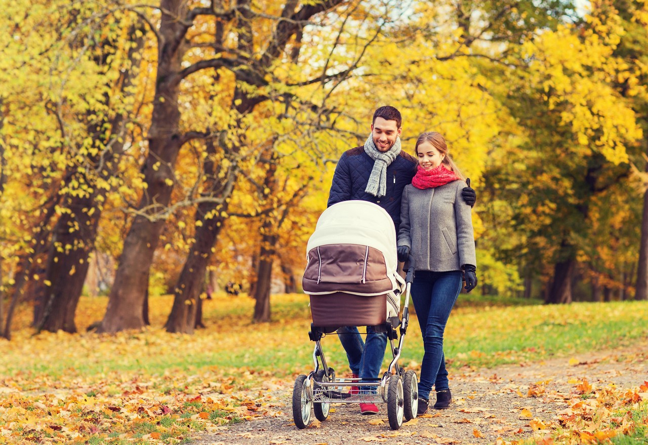 Smiling couple with baby pram in autumn park