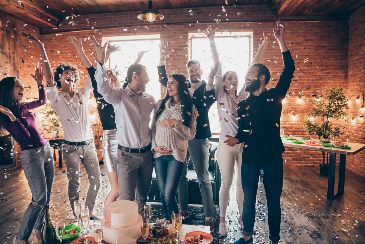 Photo of group amazing friends throwing confetti surprise baby party meeting, future parents big cake champagne snacks on table formalwear restaurant indoors