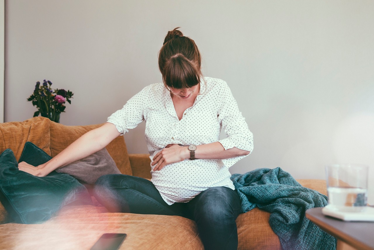 Expectant mother (9 months pregnant) timing her contractions while sitting on couch at home