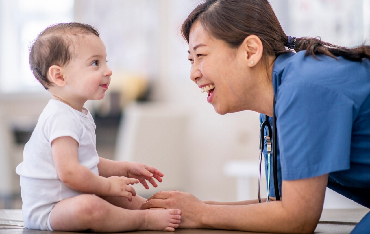 A female doctor of Asian descent is giving a baby a checkup. She is comforting and relaxed.