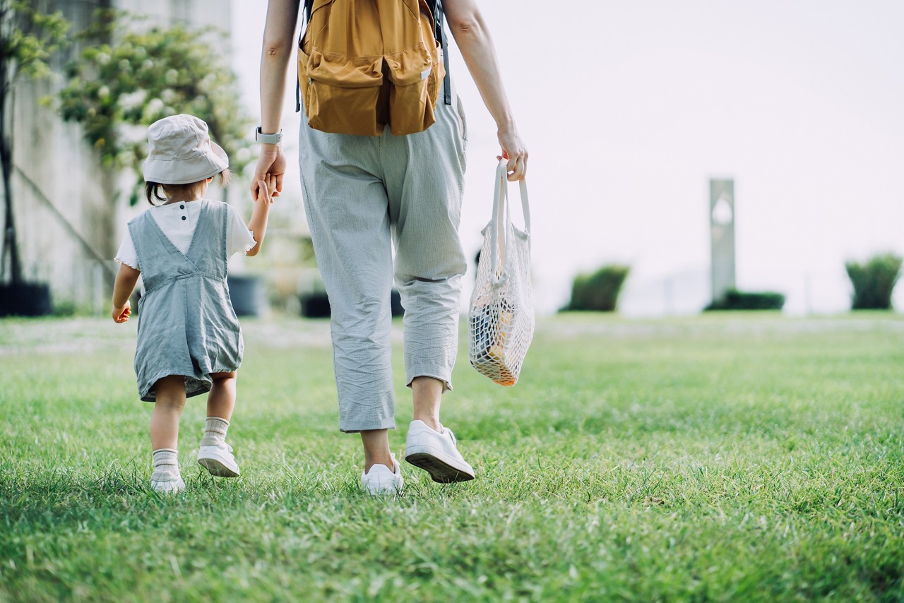 Cropped shot of young Asian mother carrying groceries with cotton mesh eco bag. Walking hand in hand with little daughter across parkland after grocery shopping together. Zero waste concept