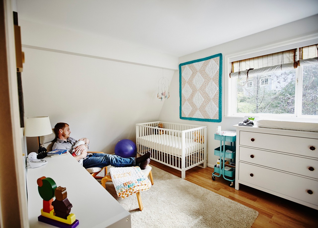 Father falling asleep while rocking baby to sleep in nursery in home