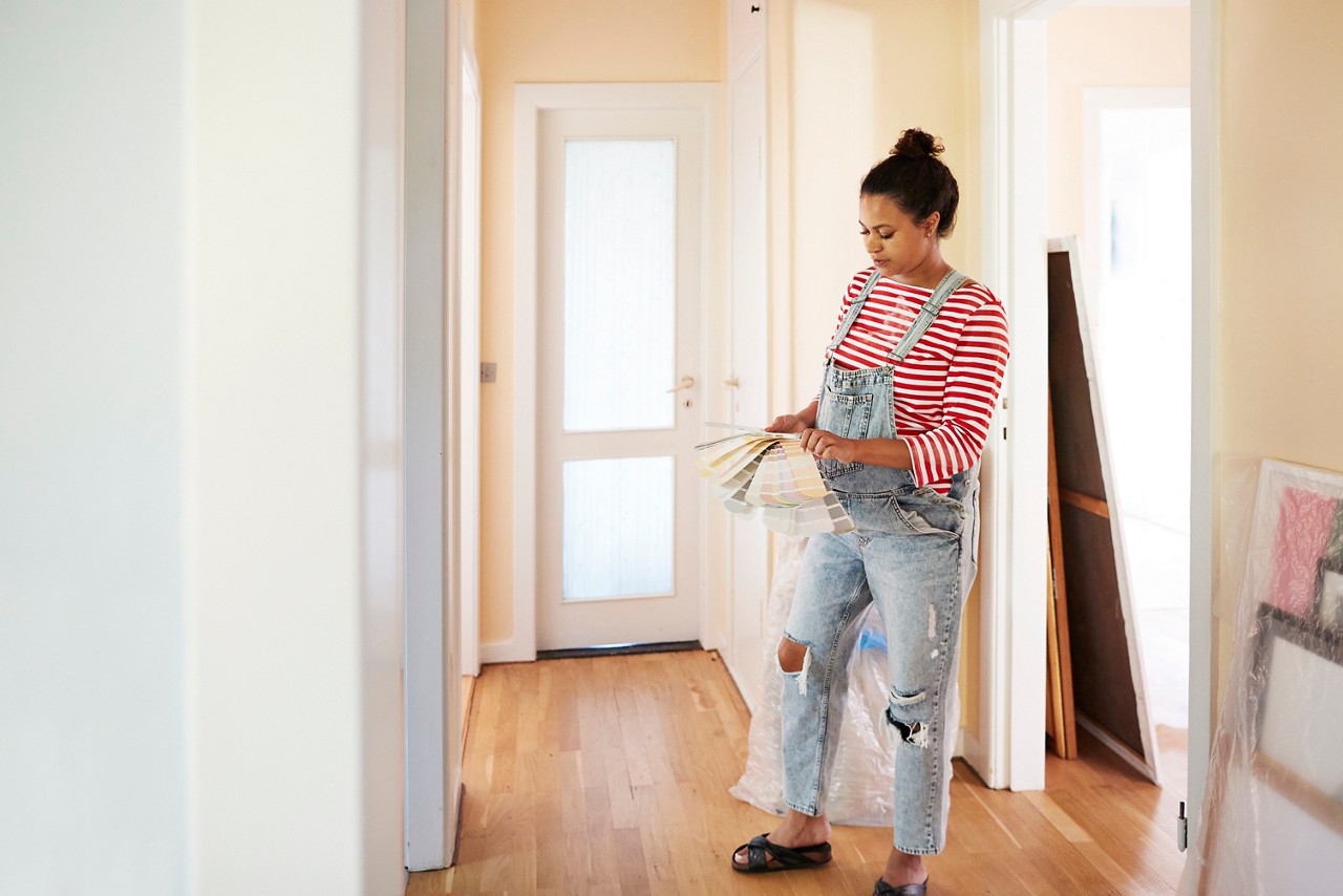 Pregnant young woman choosing paint color from swatch while standing in corridor of home