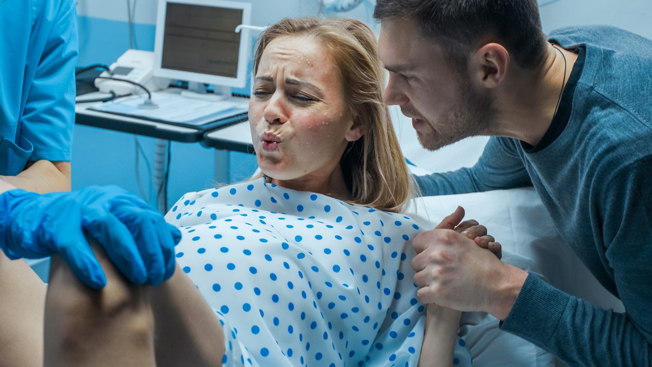 In the Hospital Close-up on Woman in Labor Pushes to Give Birth, Obstetricians Assisting, Husband Holds Her Hand. Modern Delivery Ward with Professional Midwives.