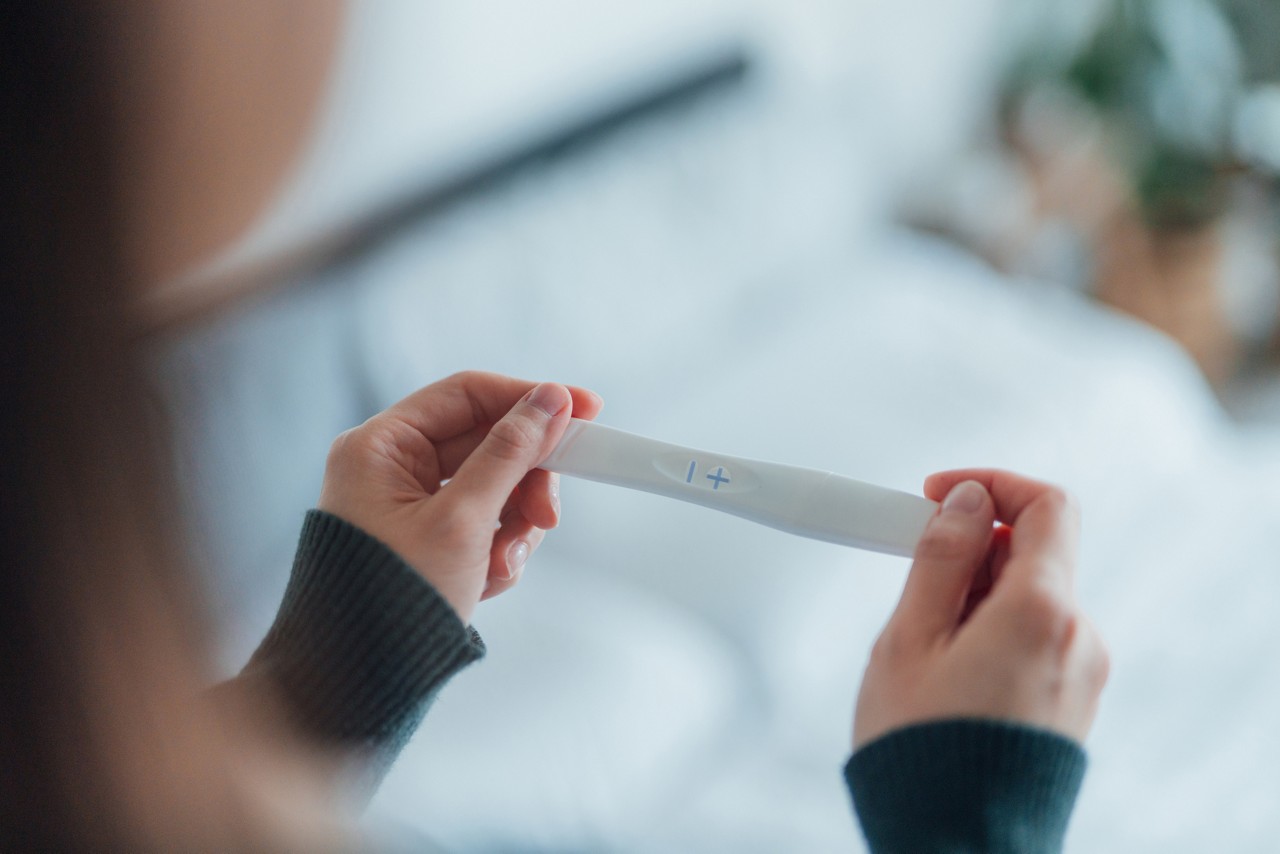 Close-up shot of unrecognisable Asian woman holding a pregnancy test kit and waiting for the result in bedroom.
