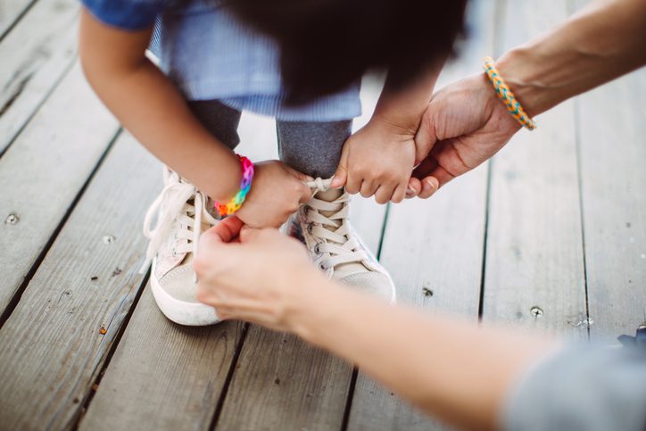 Mom helping and teaching little girl to tide up her shoelace