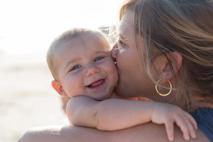 Mom kisses her baby boy on a cheek and he enjoys it very much smiling at camera.