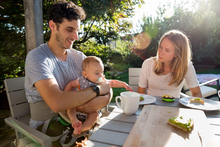 Young parents eat outside in a garden with their baby boy
