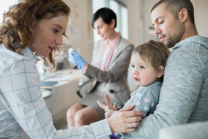 Parents holding baby girl while pediatrician prepares vaccination