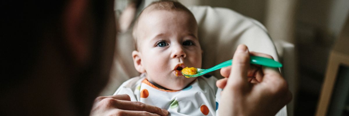 Baby wird mit orangenem Brei gefüttert