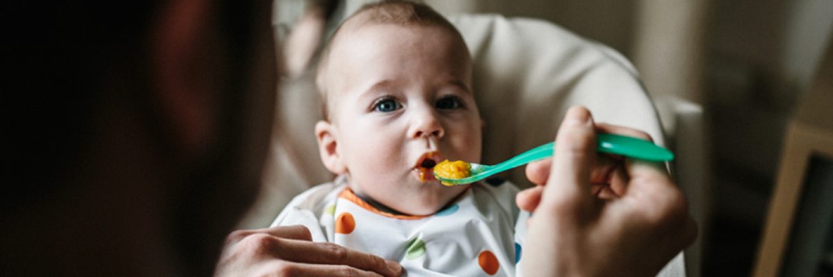 Baby wird mit orangenem Brei gefüttert