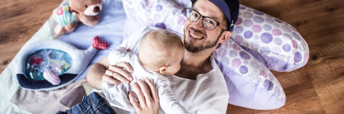 Vater liegt mit Baby auf dem Stillkissen