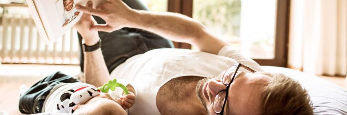 Vater liegt mit Baby auf dem Boden und liest vor