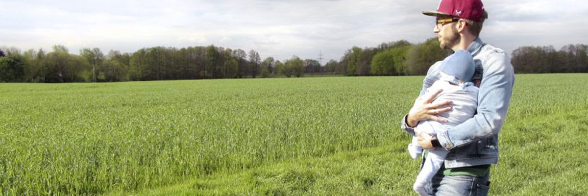 Vater hält Baby im Arm und blickt auf eine Wiese