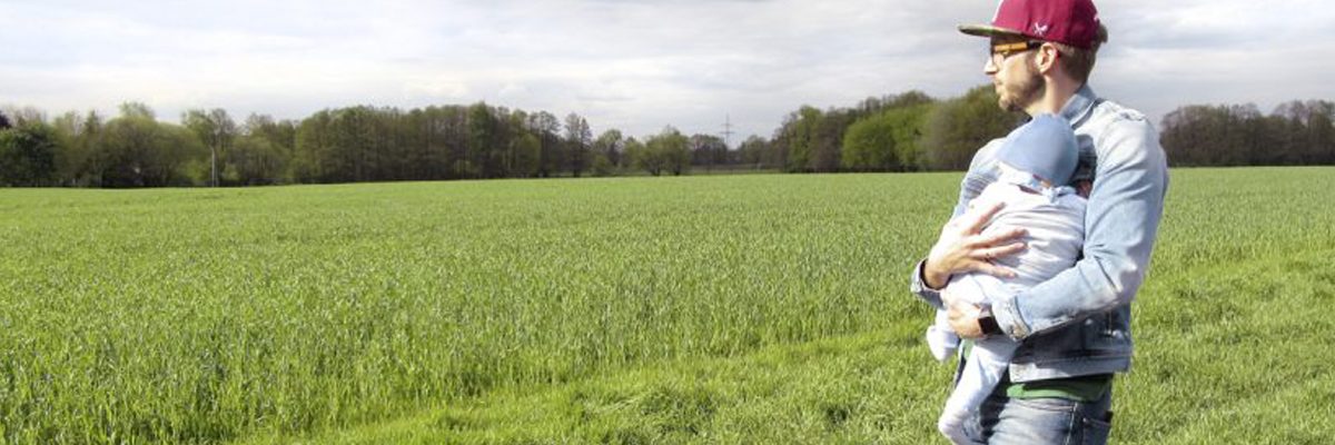 Vater hält Baby im Arm und blickt auf eine Wiese