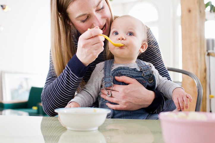 Mid adult woman feeding baby daughter at kitchen table