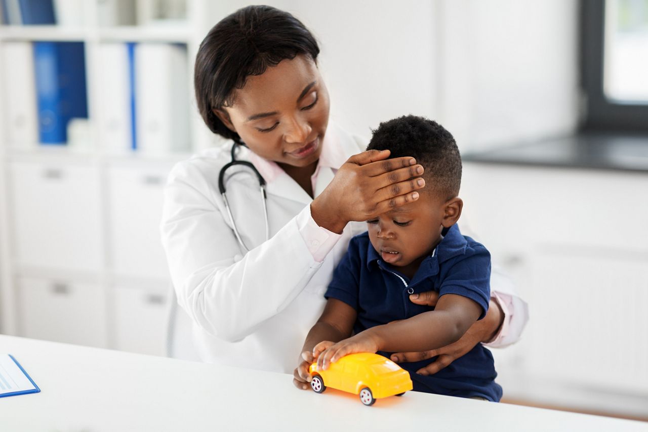 medicine, healtcare, pediatry and people concept - happy african american female doctor or pediatrician measuring baby's temperature by hand on medical exam at clinic