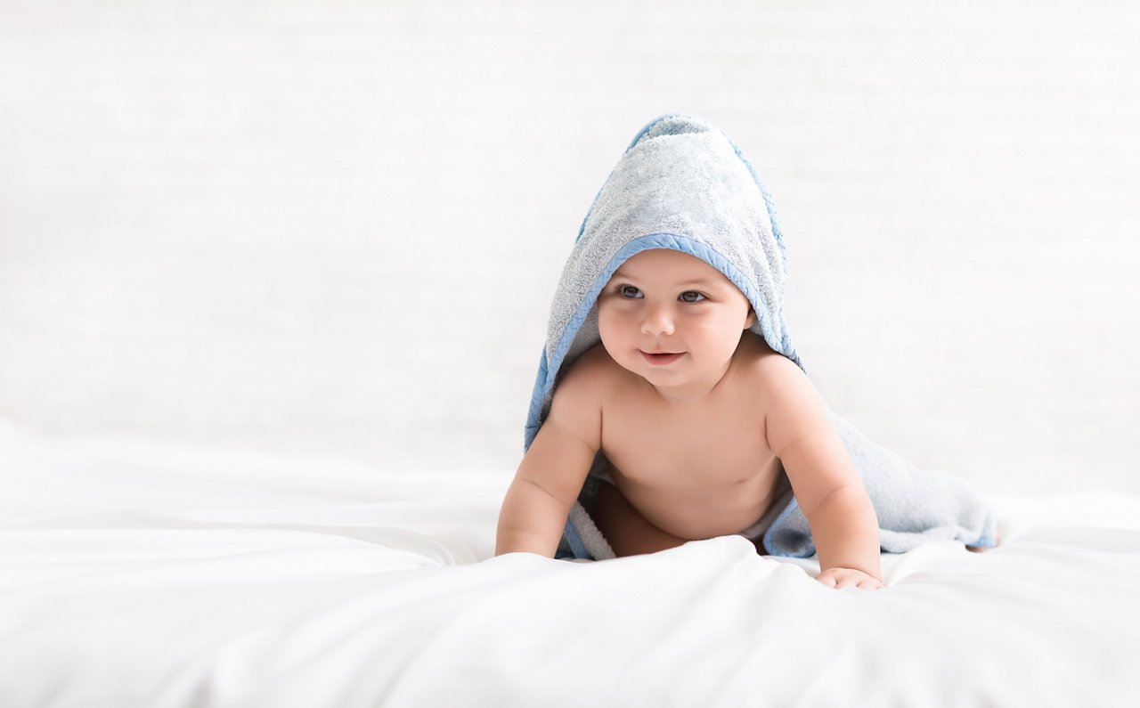 Baby crawling on bed in hooded towel