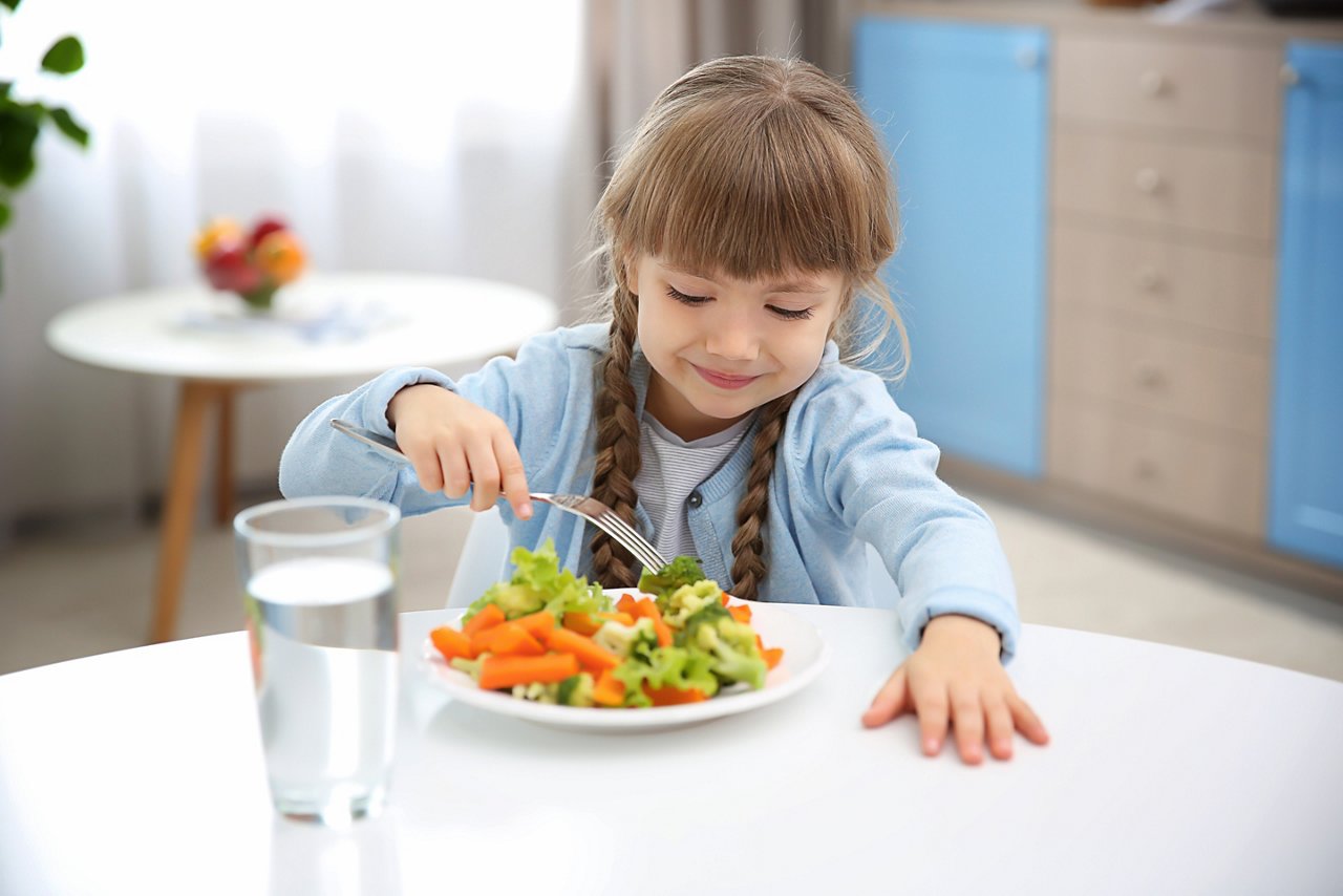 Small girl eating vegetables in kitchen