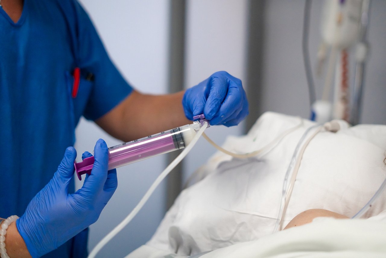 Medical professional providing a liquid meal or medication to a hospitalized patient