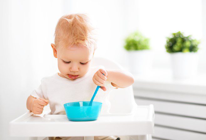 Happy baby eating himself with a spoon