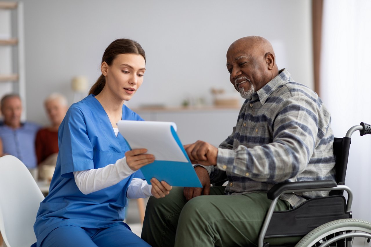 Young nurse helping senior man in wheelchair with questionnaire