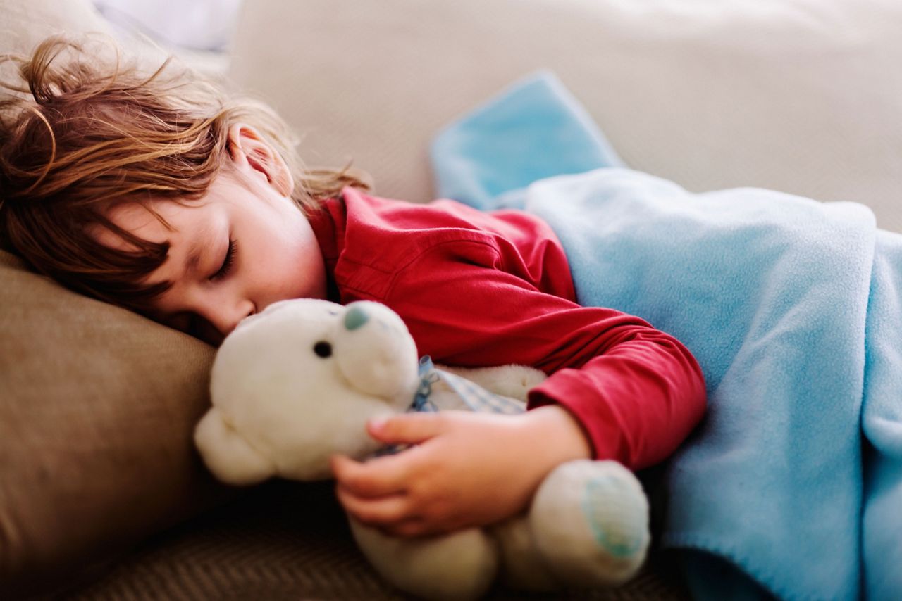Kleinkind schläft mit Teddy im Bett