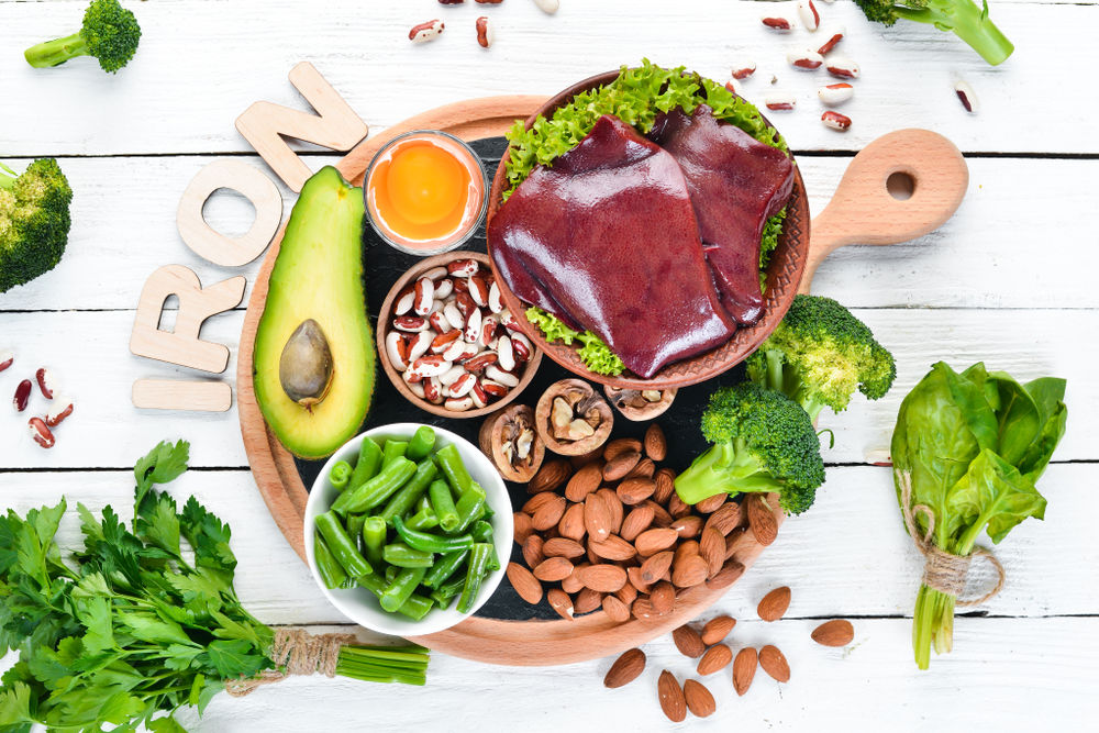 Food containing natural iron. Fe: Liver, avocado, broccoli, spinach, parsley, beans, nuts, on a white wooden background. Top view.