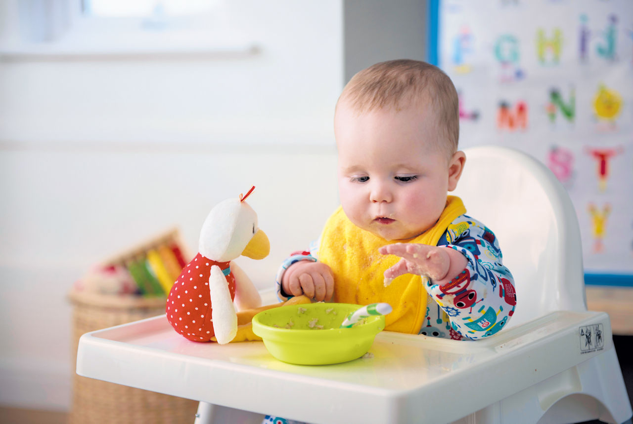 Baby sitting in highchair eating porridge