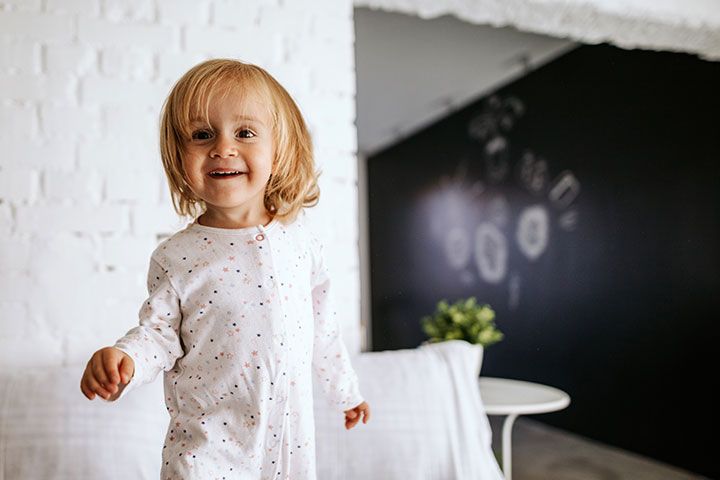Kleinkind im weißen Pyjama steht lachend