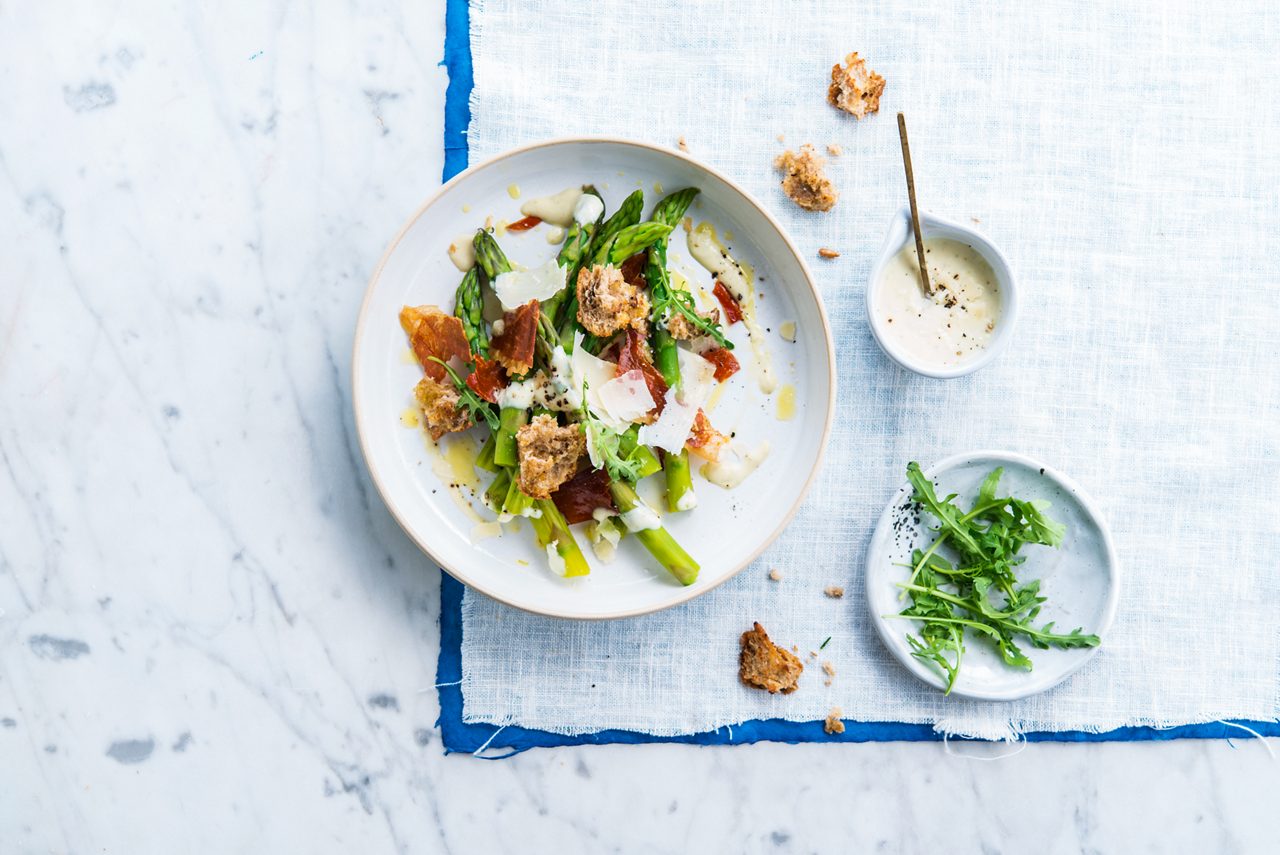 64D6020D-2625-4006-87092E008A8048D3<br>A_NA_NA_Master_Recipe_Image_asparagusganda___PBAY_NA_Soy_NA_Pot_500g_HR_horizontal.tif<br>Green Asparagus with Crispy Ganda Ham and Parmesan

A deliciously savoury, seasonal starter for summer with Alpro Simple Plain

"24 green asparagus spears 
100g rocket 
50g Alpro Soya Baking and Roasting 
8 slices Ganda ham / Cured ham (prosciutto) 
2 slices brown bread
30g Parmesan
For the dressing: 
4 tbsp Alpro Simple Plain
10g Parmesan, grated 
2 tsp mustard 
1 lime, juice and zest
A few drops of truffle oil 
Freshly ground black pepper & sea salt"

"1.	Prepare the toppings. Heat your oven to 200°C. Spread the Ganda/cured ham/prosciutto between two sheets of baking paper and dry them in the oven for 20 minutes until crispy. Grate or process the bread slices to make breadcrumbs, rub together with 1 tbsp Alpro Soya Baking and Frying and bake in the oven until golden brown. 
2.	Cook the asparagus. Clean and peel the spears and remove the hard, thick ends. Bake them in the remaining Alpro Soya Baking and Roasting until al dente and season with freshly ground pepper.
3.	Make the dressing: Mix the Alpro Simple Plain together with 10g grated Parmesan, the mustard, lime juice and zest, pepper and salt. 
4.	Serve the baked asparagus topped with shavings of Parmesan, the dried Ganda/cured ham/prosciutto and rocket. Drizzle on the dressing and finish with a few luxurious drops of truffle oil, the bread crumble and a twist of sea salt."