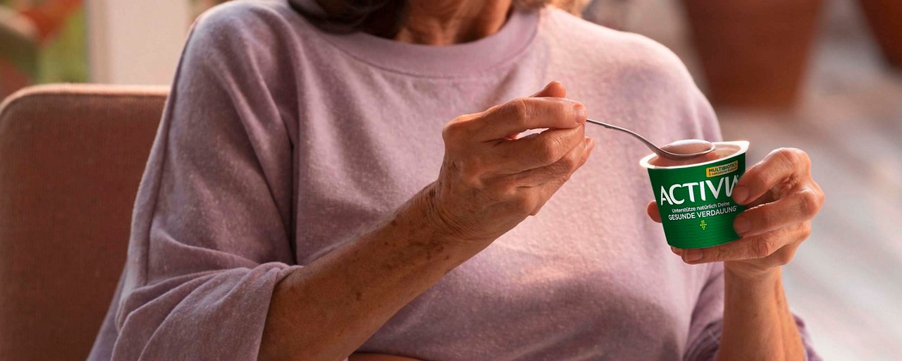 Frau in rosa Pullover isst Activia