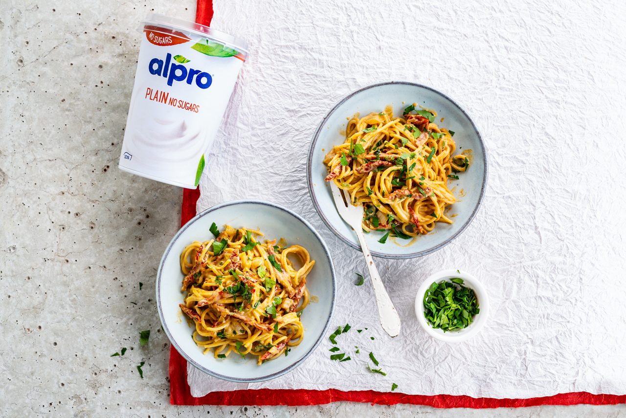 C945061D-7EE6-495E-902C7E8123FDF12D<br>A_GFY_NA_Master_Recipe_Image_vegancarbonarapackshot___PBAY_NS_Soy_Plain_Pot_500g_HR_horizontal.tif<br>Vibrant vegan Pasta Carbonara

400g wholewheat pasta
16 sun-dried tomatoes (the dry ones, not in oil)
2 tsp soy sauce
2 tsp smoked paprika powder
1 tbsp olive oil
1 onion, finely chopped
2 cloves of garlic 
A handful of fresh parsley leaves, 
200ml Soya Plain No sugars plant-based alternative to yogurt 
3 tbsp nutritional yeast powder
Salt
Black pepper

"Preheat the oven to 180 °C.
Cut the sun-dried tomatoes into thin strips, mix with soy sauce and smoked paprika powder. Lay on a baking dish and bake in the oven for 2 to 3 minutes.
Meanwhile, cook the pasta al dente according to the instructions on the package.
Heat oil in a large saucepan over medium heat. Bake the finely chopped onion and garlic until the onion is translucent. Drain the pasta but keep 80 ml of cooking water. 
Add to the pasta, sun-dried tomatoes, the onion and mix in the Alpro Plain No Sugars, cooking water and nutritional yeast. Mix well and season with pepper and freely with extra salt.
Serve immediately with parsley."