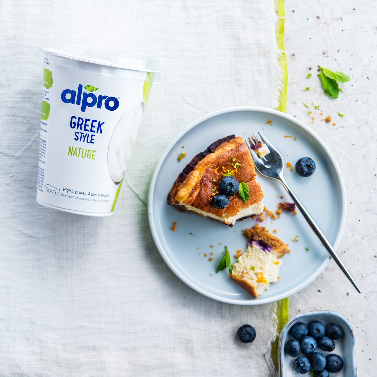 E1095801-CADB-49C8-96955AEDD2E4941F<br>A_NA_NA_Master_IG_Image_blueberrycakepackshot___GreekStyle_NA_Soy_NA_Pot_400g_HR_1x1.tif<br>Tender Blueberry Cake

A luscious melt-in-your-mouth cake with creamy textured Alpro Plain Soya alternative to Greek Style yogurt

"180g biscuits
50g melted Alpro Baking & Frying
800g Alpro Plain Soya alternative to Greek Style yogurt80g cane sugar 
100ml vegetable oil (sunflower oil or rapeseed oil) 
4 eggs
250g blueberries 
2 mandarins 
1 vanilla pod 
1 lime "

"1. Creamy on top, crunchy underneath, fruity all the way through! Preheat the oven to 180 °C and grease the sides of a cake tin. Crush the cookies and mix them with melted Alpro Baking & Frying Margarine then spread evenly over the base of the tin. Keep cool until you’re ready to use.
2. Whisk the Alpro Plain Soya alternative to Greek Style yogurt with the cane sugar, oil and egg yolks until it’s smooth and creamy. Add the seeds from the vanilla pod, the lime zest and 2 tablespoons of lime juice and mix in. Add extra lime or vanilla if you think it needs it. 
3. Whisk the egg whites until stiff and gently fold in the Alpro mixture, keeping it light and fluffy. Arrange the mandarins and half of the blueberries over the biscuit base. Then scoop the Alpro Plain Soya alternative to Greek Style yogurt filling over the top and bake in the preheated oven for 40-45 minutes until the top of the cake is golden brown. 
4. After it cools down, decorate with the rest of the blueberries and a sprig or two of mint. Stand back and admire. You made that! "