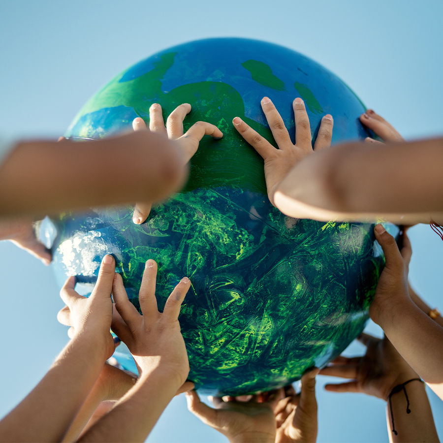 Image of a toy globe being held by the hands of several children. 