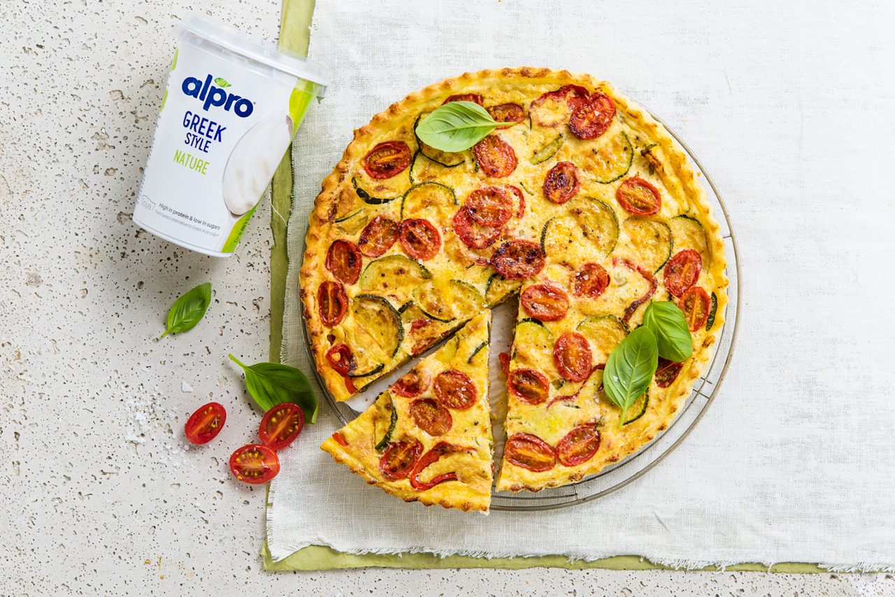 B0A40765-602E-40E8-A9D8B0F0F42308E4<br>A_NA_NA_Master_Recipe_Image_mediterraneanquichepackshot___GreekStyle_NA_Soy_NA_Pot_400g_HR_horizontal.tif<br>Colourful Mediterranean Quiche

A quick and easy quiche packed with flavour, with Alpro Plain Soya alternative to Greek Style yogurt

1 pack ready-made short crust pastry, chilled
400g  Alpro Plain Soya alternative to Greek Style yogurt
1 courgette 
1 sweet red pepper 
125g cherry tomatoes 
3 eggs
2 tbsp red pesto 
40g Parmesan, grated
Alpro Margarine for Baking and Frying
Handful of fresh basil
Nutmeg
Freshly ground pepper and salt

"1.	Preheat the oven to 180ºC and get a 10” loose bottomed, fluted flan tin out and prepped ready. 
2.	Make your quiche filling. Chop the courgette and sweet peppers. Heat a little Alpro Margarine for Baking and Frying in a skillet and fry the veg for about five minutes. Season with pepper and salt. Put the Alpro Plain Soya alternative to Greek Style yogurt and the three eggs in a bowl and whisk well. Add half the grated Parmesan and a few chopped basil leaves. Stir and season with nutmeg, freshly ground pepper and salt. Cut the cherry tomatoes in half and put to one side.
3.	Now for the case. Remove the pastry dough from the fridge and roll it out on a clean, floured surface. Position over the tin and ease it in gently, pressing against the base and sides to get a good fit. Trim off any excess from around the top. Prebake if necessary, according to the instructions on the pack.
4.	And… assemble. Brush the pastry base with the pesto and spread the cooked veg over the top. Pour over the cheesy Alpro mixture and sprinkle with the rest of the grated Parmesan cheese. Cover with the halved cherry tomatoes and bake for about 45 minutes until golden-brown. Slice into segments and serve with fresh basil leaves and a green salad. Bright, vibrant and full of Mediterranean sunshine. "