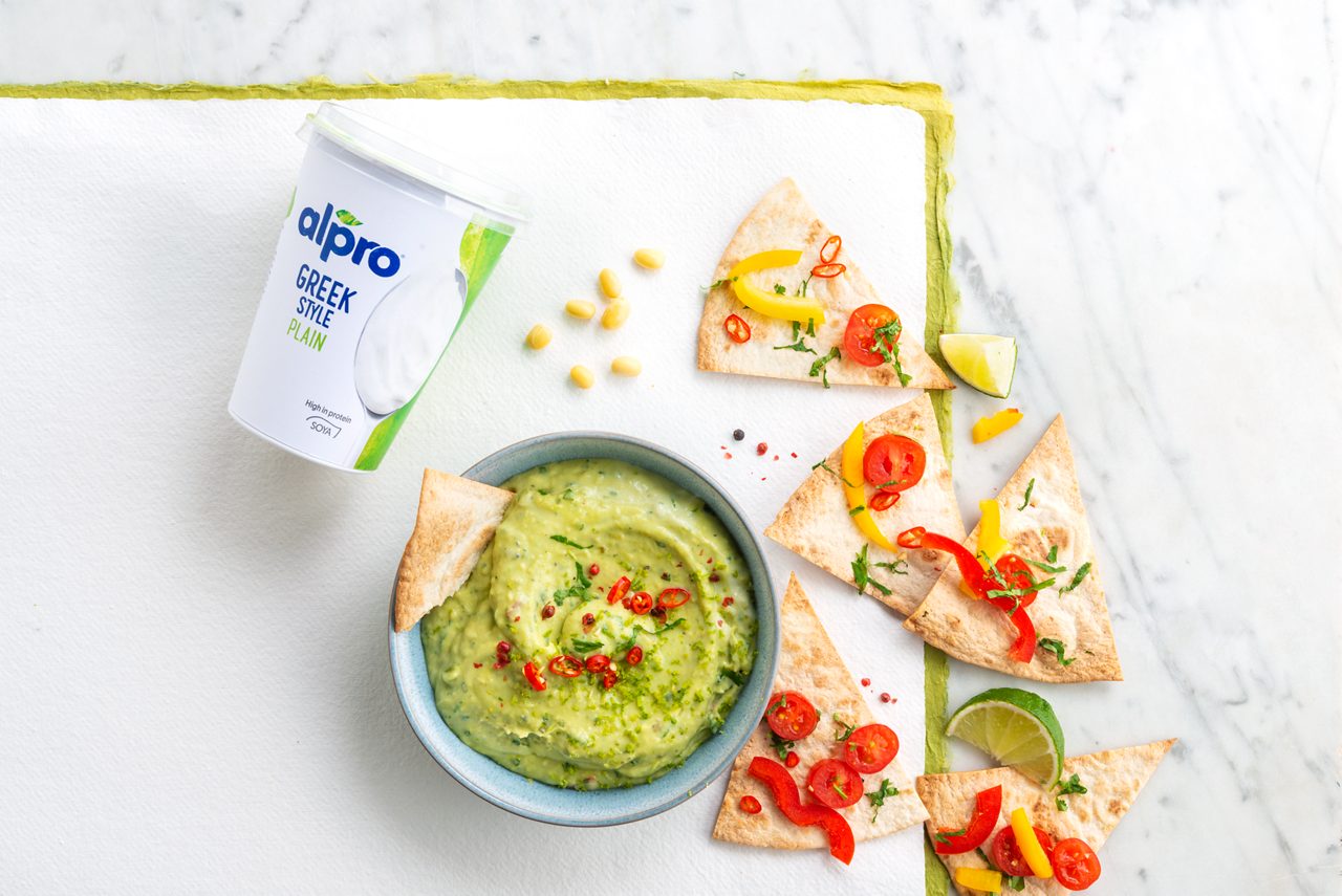 D6A4AAF2-17EA-48A2-AEF10E2E75A1F9E2<br>A_GFY_NA_MASTER_Recipe_Image_NachosAvocadoDip___Greekstyle_NA_Soy_NA_Pot_500g_HR_horizontal-44.tif<br>Crunchy nachos with avocado dip  
Tastes as colourful as it looks! The perfect summer appetiser, with an Alpro’n’avocado dip 
"For the avocado dip: 
2 avocados, sliced 
4 sprigs of coriander 
1 lemon 
200gr Alpro plant-based alternative to Greek Style yogurt Plain 
¼ tsp cumin 
¼ tsp salt 
¼ tsp black pepper 
2 fresh red chillies
For the nachos: 
6 wraps 
10 cherry tomatoes 
2 spring onions 
2 sweet peppers (1 yellow, 1 red) "
"1. First off, heat your oven to 200º. 
2. Then do the dip. Chop the coriander leaves and add the zest from one half of the lemon and the juice from the other half, then add to the  Alpro plant-based alternative to Greek Style yogurt Plain along with the sliced avocados and mix well until it’s smooth. Season with the cumin, salt and pepper, pour into a bowl and garnish with the thinly sliced chillies.
 3. Now for the nachos. Cut each wrap into 8 triangular slices, spread them out on a baking tray and season with salt & pepper. Bake for 15 minutes at 200°C, turning them over after 8 minutes until they’re crispy and golden. 
4. Arrange the warm nachos on a large plate or platter, garnish with chunks of tomato, the sliced spring onion and peppers. Serve with the dip and get  stuck in and sharing!"
(Recipe type: Appetizer (Prep time: 10 min) (baking time: 15 min) (servings: +/- 4 persons) (season: all year) (pool: 1)