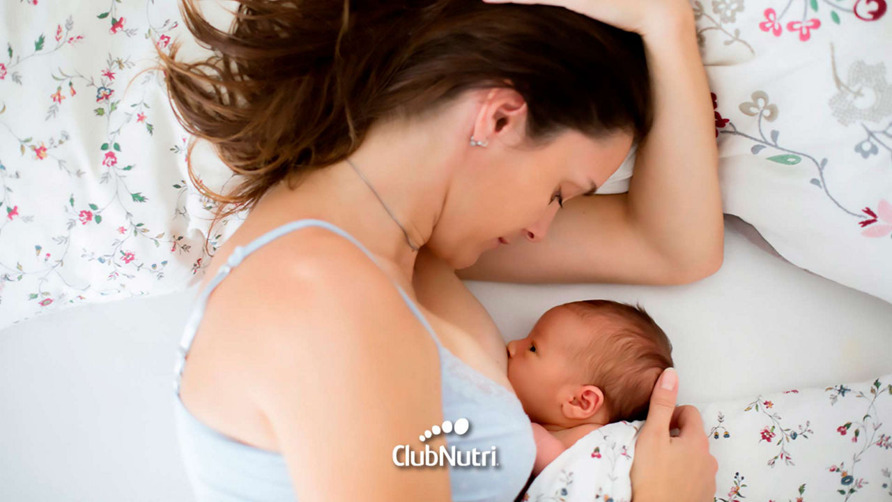 Madre recostada en la cama amamantando a su bebé durante la noche, resaltando el vínculo y la nutrición nocturna.