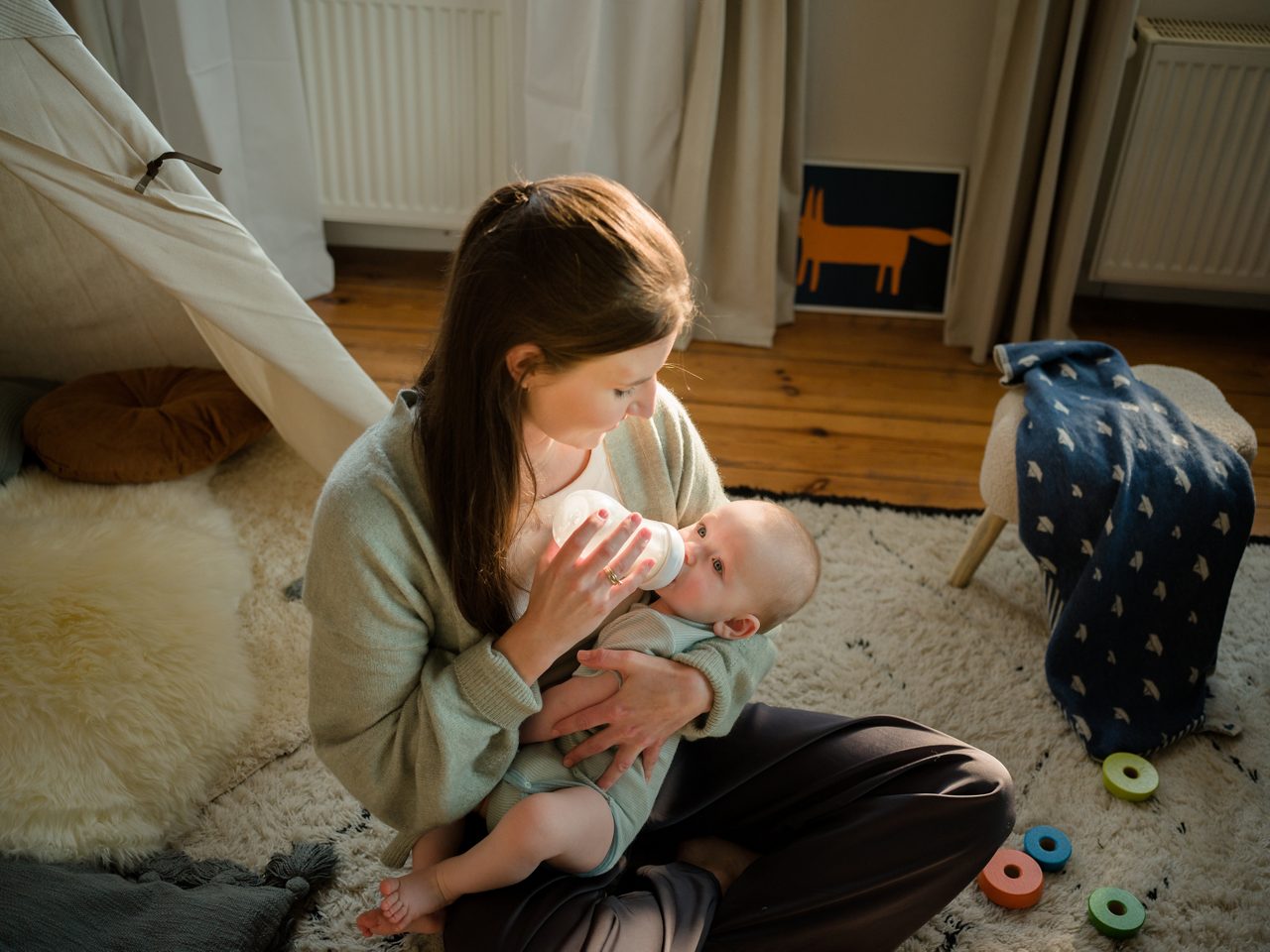 Persoon geeft een baby een fles in een comfortabele thuisomgeving, wat babyvoeding en dagelijkse zorg voor jonge kinderen illustreert.