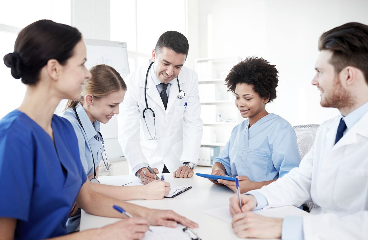 medical education, health care, people and medicine concept - group of happy doctors or interns with mentor meeting and taking notes at hospital