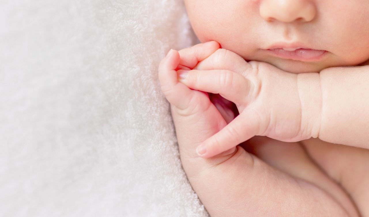 tender lips and nose and crossed fingers of a newborn baby asleep on a diaper, closeup