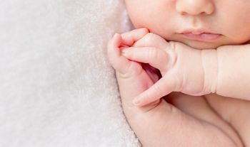 tender lips and nose and crossed fingers of a newborn baby asleep on a diaper, closeup